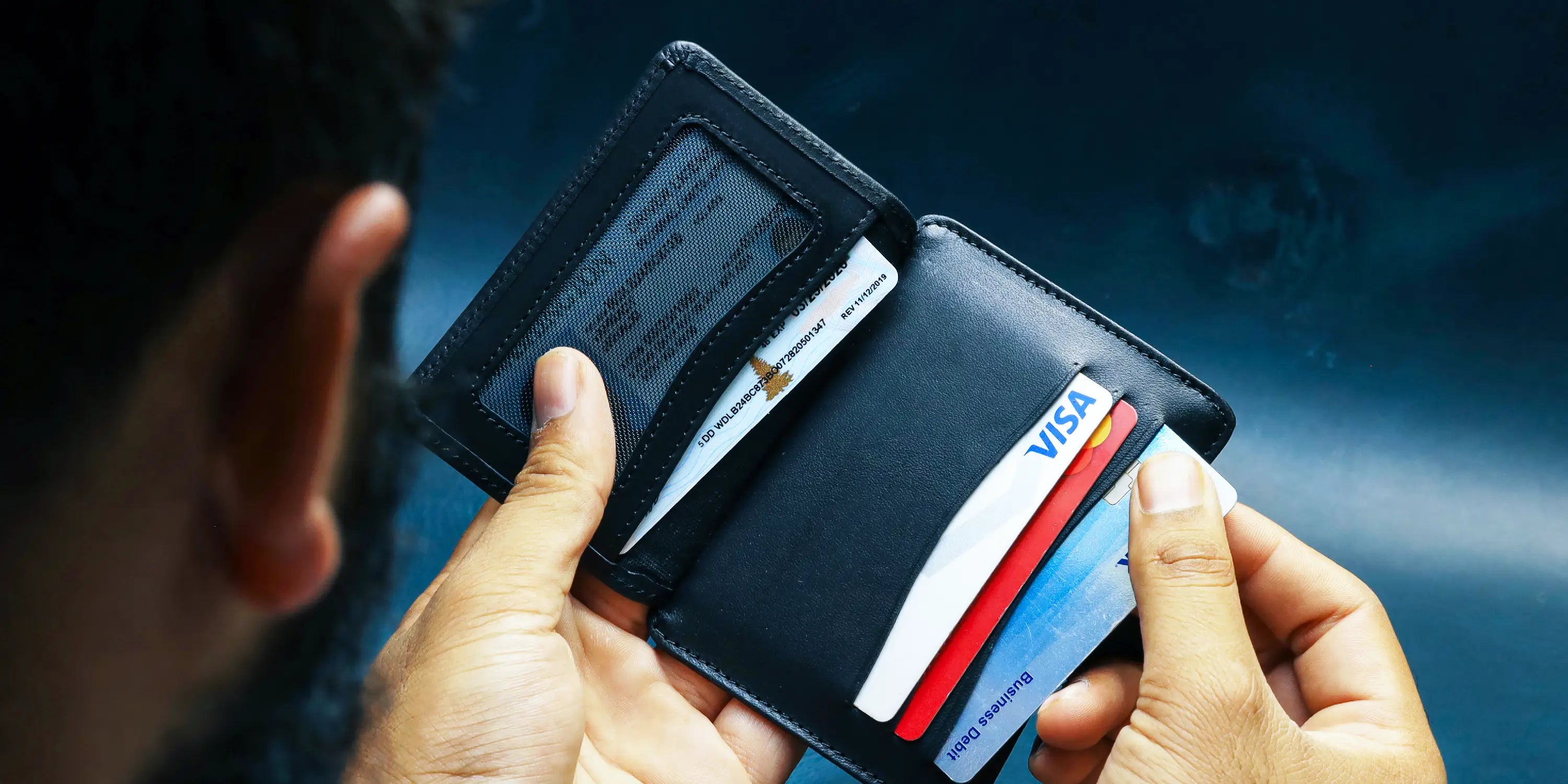 Man pulling a card from a lapis color handmade leather card holder.