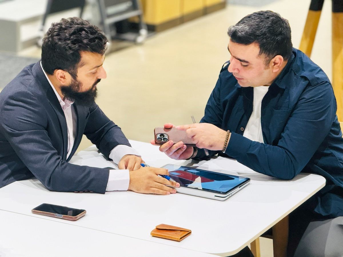 Deerhandmade founders talking about leather goods, with some products in hand and others on the table.